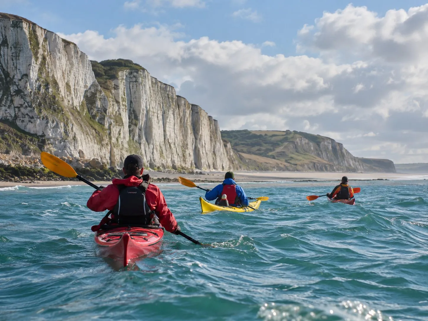 Trois kayaks de mer sur l’eau, au pied des falaises blanches