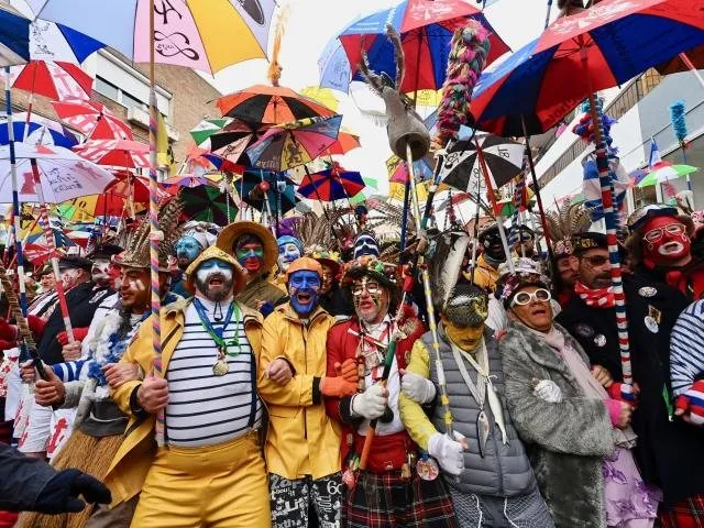 Costumed, made-up revellers, umbrellas held above the bande