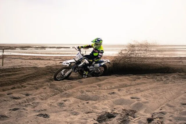 Een coureur op volle snelheid in het zand, met een zandwolk achter zich