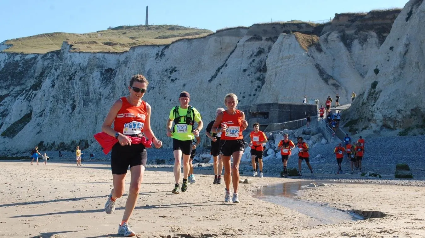 Drie lopers met startnummer op de buik, op het zand